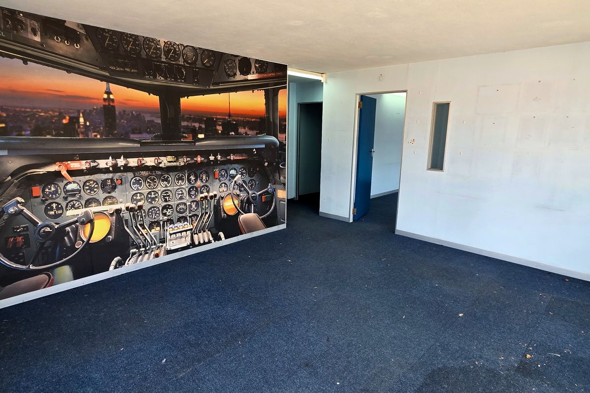 An empty office space featuring blue carpet flooring and a large wall mural, requiring cosmetic updates to the walls and flooring.