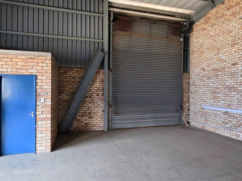 Spacious industrial utility area featuring exposed brick walls, concrete flooring, and a large roller shutter door for easy access.