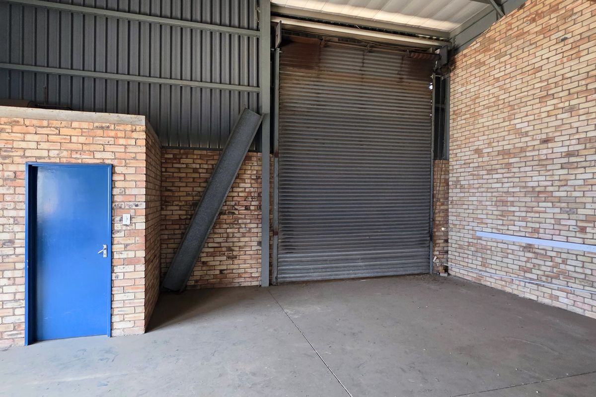 Spacious industrial utility area featuring exposed brick walls, concrete flooring, and a large roller shutter door for easy access.
