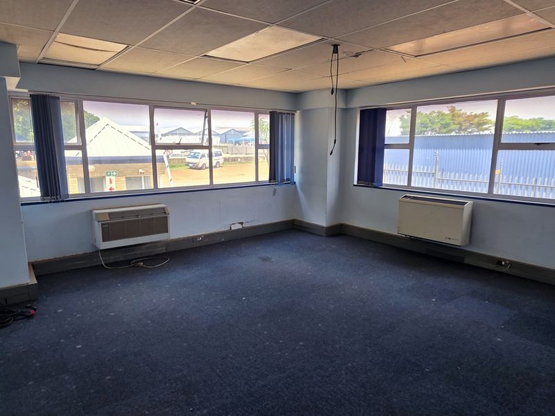 An empty office space featuring carpet flooring, suspended ceiling tiles, and window-mounted air conditioning units, suitable for a professional workspace.