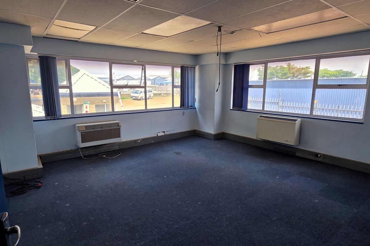 An empty office space featuring carpet flooring, suspended ceiling tiles, and window-mounted air conditioning units, suitable for a professional workspace.