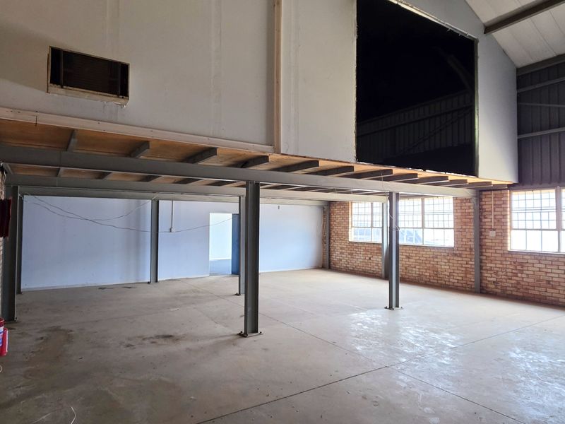 Spacious industrial open-plan area featuring exposed steel beams, a mezzanine level, brick walls, and large windows, offering a versatile blank canvas for commercial use.