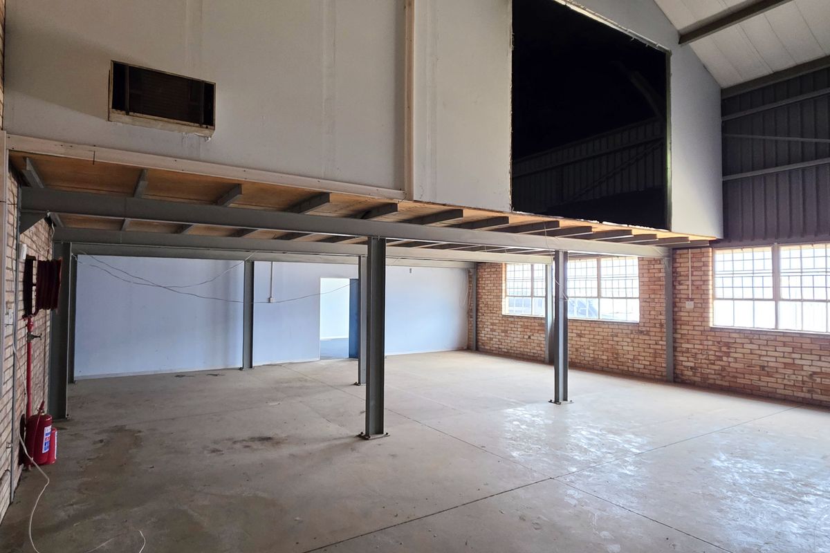 Spacious industrial open-plan area featuring exposed steel beams, a mezzanine level, brick walls, and large windows, offering a versatile blank canvas for commercial use.