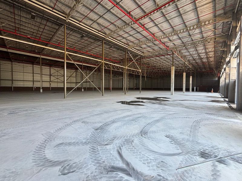 Expansive industrial warehouse space featuring high ceilings, exposed steel portal frame construction, fire sprinkler system, and durable concrete flooring.