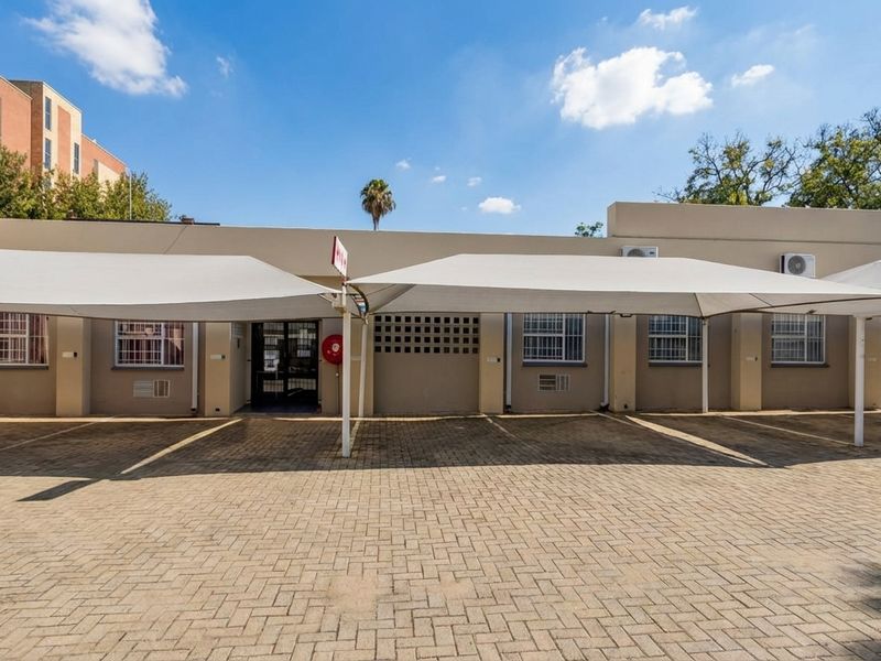 Exterior view of a commercial building featuring a paved parking area with shade sail structures and security bars on windows.