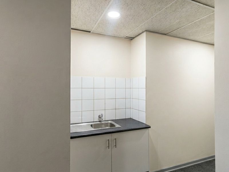 A compact kitchenette area featuring a stainless steel sink, laminate countertop, white tiled splashback, and base cabinetry.