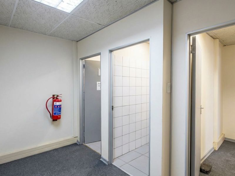 A functional office hallway featuring carpeted flooring, drop ceiling panels, and access to multiple utility or office rooms.