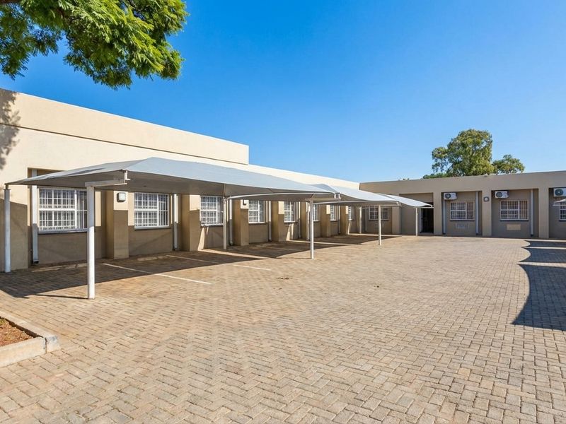 Exterior view of a commercial property featuring a paved parking area with covered shade-net carports and wall-mounted air conditioning units.