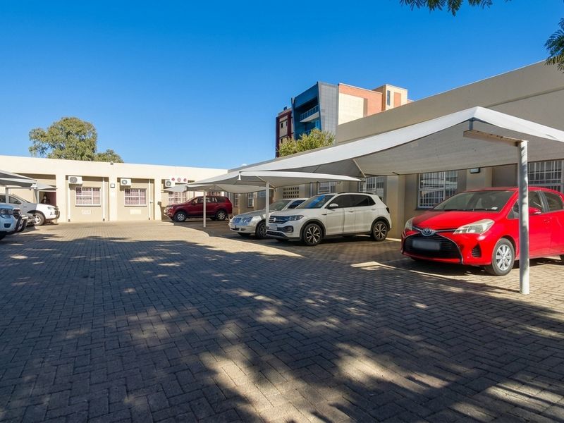 Exterior view of a commercial property featuring a paved parking area with multiple shade-cloth carports and building access points.