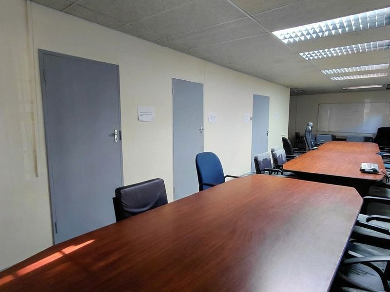 A functional office meeting room featuring multiple entry doors, recessed fluorescent lighting, and a large whiteboard, suitable for professional business operations.