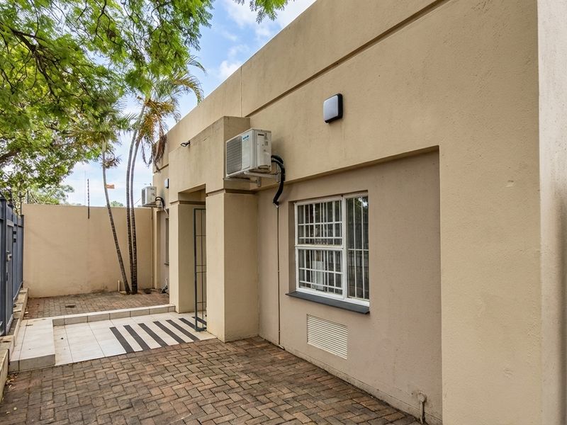 Rear exterior view of the business property featuring paved courtyard area, security fencing, and wall-mounted air conditioning units.