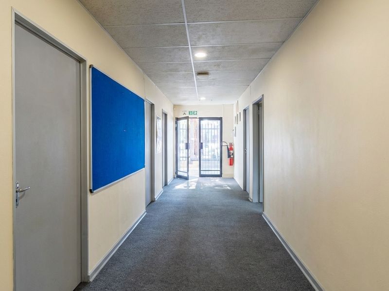 A functional commercial hallway featuring carpeted flooring, multiple access doors, and a secure exterior entrance with a security gate.