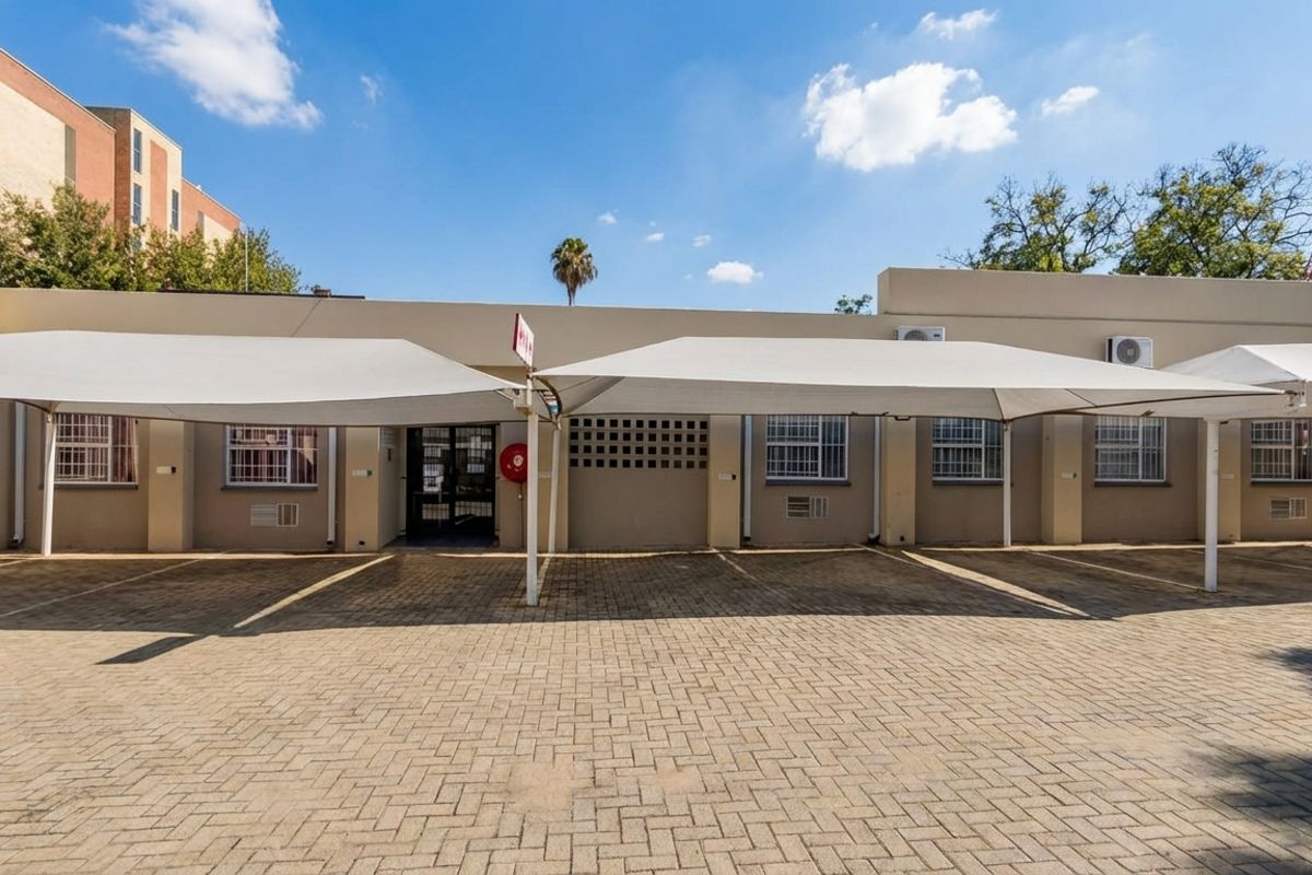 Exterior view of a commercial building featuring a paved parking area with shade sail structures and security bars on windows.