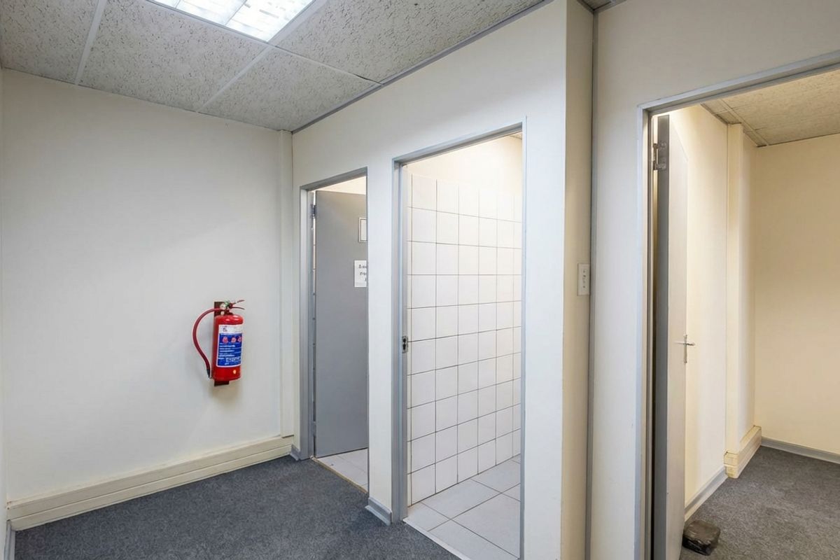 A functional office hallway featuring carpeted flooring, drop ceiling panels, and access to multiple utility or office rooms.