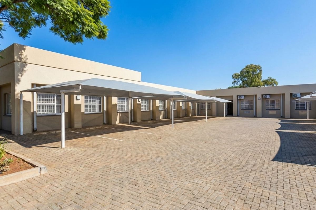 Exterior view of a commercial property featuring a paved parking area with covered shade-net carports and wall-mounted air conditioning units.