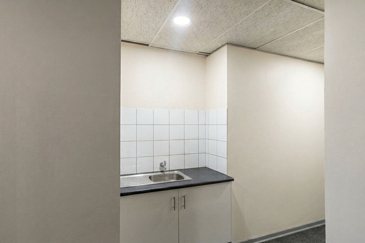 A compact kitchenette area featuring a stainless steel sink, laminate countertop, white tiled splashback, and base cabinetry.