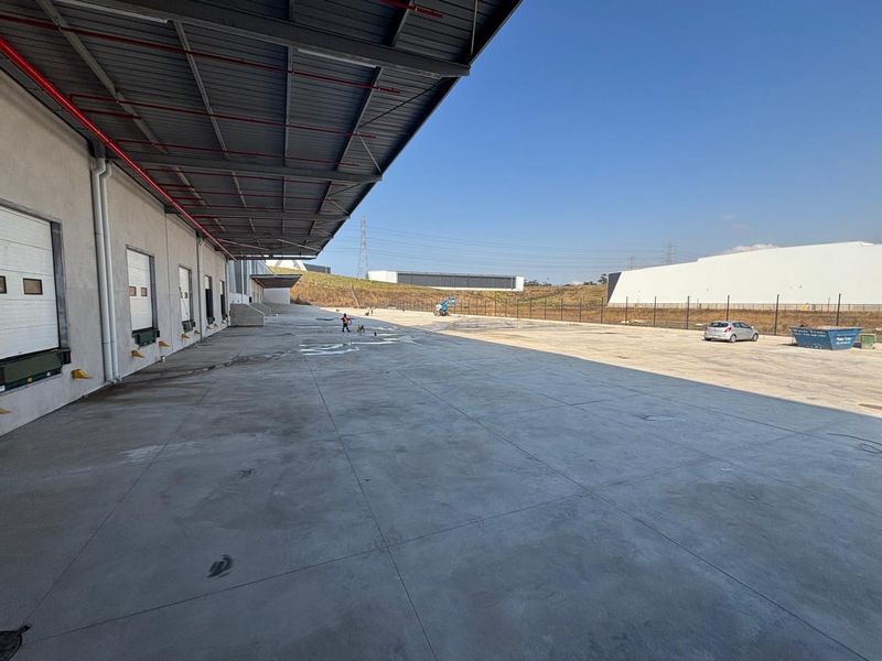 Spacious industrial concrete yard featuring multiple loading docks under a large metal canopy, suitable for logistics and heavy vehicle operations.