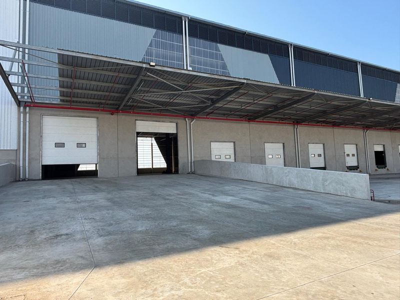 Industrial warehouse exterior featuring multiple roller shutter loading doors, a concrete loading bay, and a large steel-framed canopy structure.