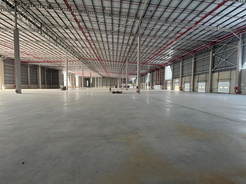 Expansive industrial warehouse space featuring high ceilings, polished concrete flooring, exposed fire suppression systems, and multiple roller shutter access doors.