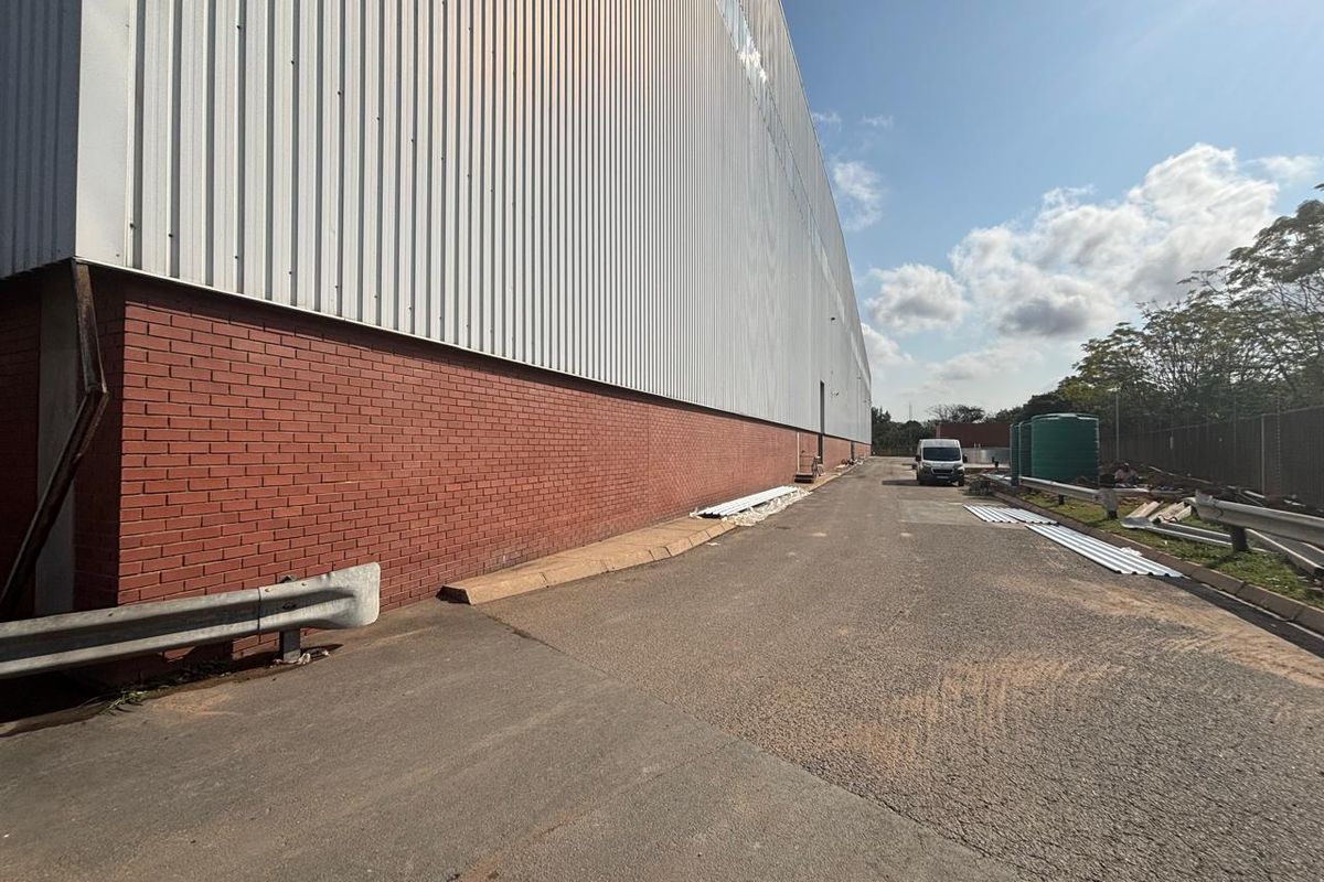 Exterior view of an industrial warehouse featuring a brick and corrugated metal facade with an adjacent asphalt driveway and water storage tanks.