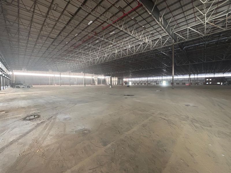 Expansive industrial warehouse space featuring high ceilings with exposed steel trusses, sprinkler systems, and durable concrete flooring, suitable for logistics or manufacturing operations.