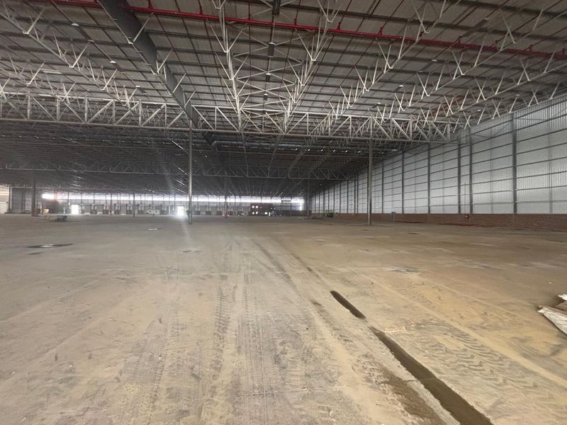 Expansive industrial warehouse space featuring high ceilings with exposed steel trusses, a fire sprinkler system, and durable concrete flooring.