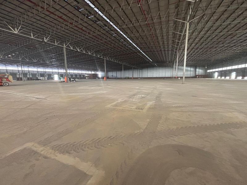 A vast, open-plan industrial warehouse space featuring high-clearance steel truss ceilings, concrete flooring, and an integrated fire sprinkler system.