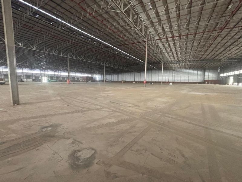 Expansive industrial warehouse space featuring high ceilings with exposed steel trusses, a fire sprinkler system, and durable concrete flooring.
