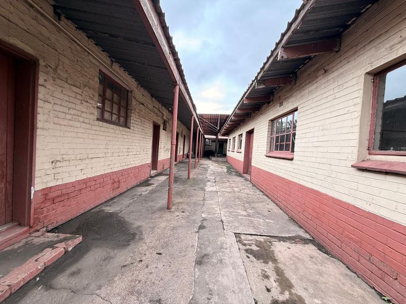 An exterior view of an industrial corridor featuring brick walls, concrete flooring, and metal support structures connecting multiple building units.