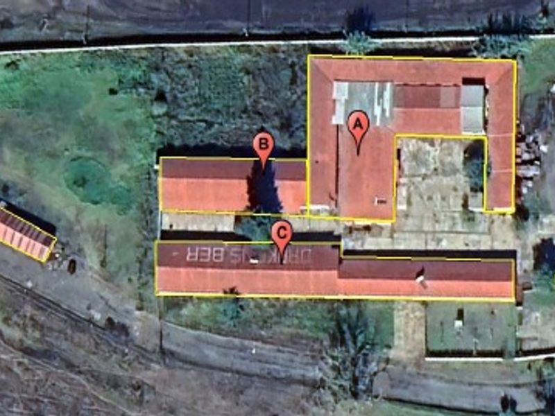 Aerial view of an industrial property complex featuring multiple warehouse structures, paved yard areas, and surrounding land.