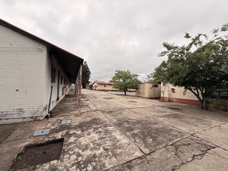 Expansive industrial yard area featuring concrete paving, covered walkways, and multiple single-story brick structures.