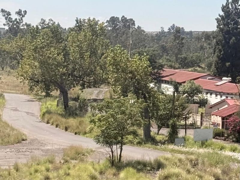 An elevated view of an industrial property site featuring access roads, mature trees, and existing warehouse-style buildings with metal roofing.