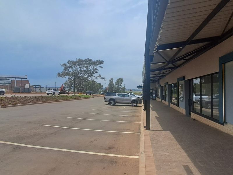 Exterior view of a retail property featuring a paved parking area and a covered walkway leading to glass storefronts.