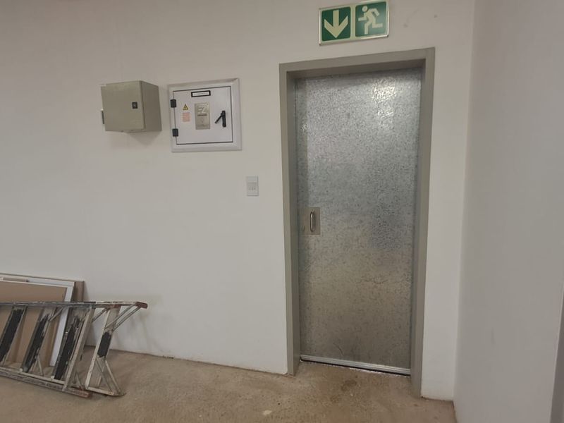 A functional utility space featuring a heavy-duty steel fire door, emergency exit signage, and wall-mounted electrical distribution infrastructure.