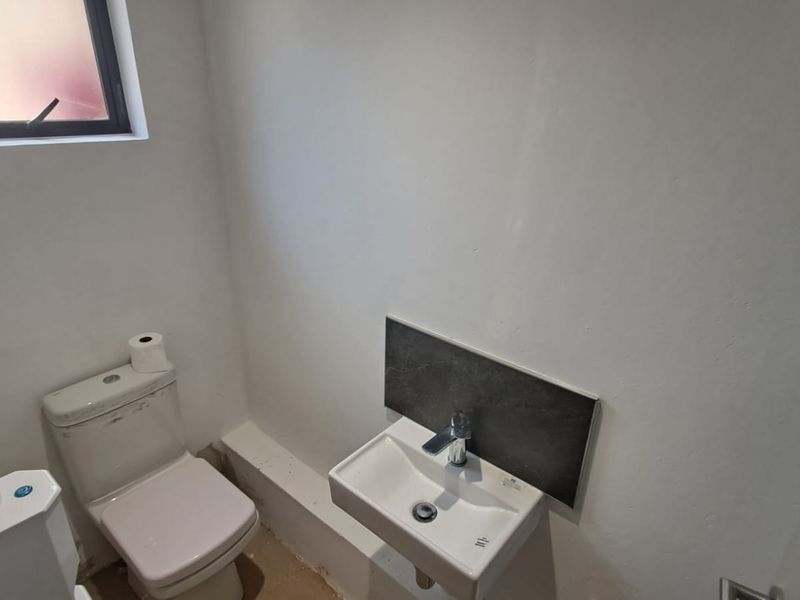 A compact bathroom featuring a white toilet and a wall-mounted basin with a dark tiled splashback, currently requiring final floor finishing.