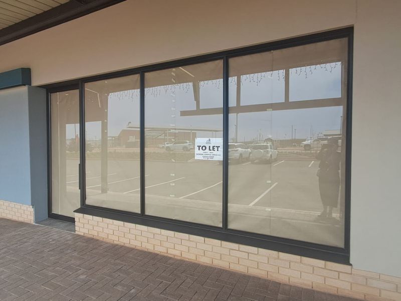 A modern retail storefront featuring large glass display windows, a brick base, and a paved walkway in a well-maintained commercial complex.