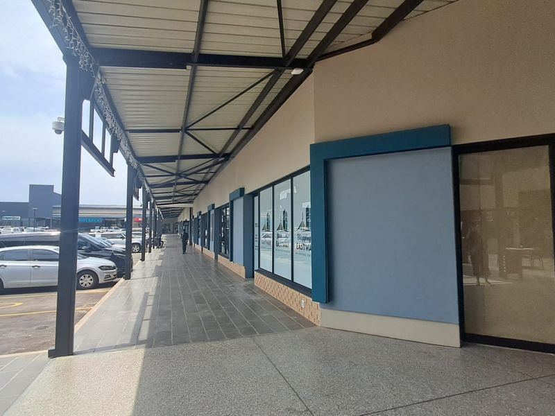A view of the retail storefronts featuring a covered walkway, large glass display windows, and paved pedestrian access in a shopping center environment.