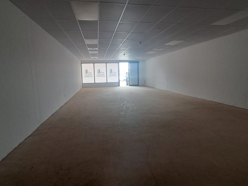 An empty, open-plan retail space featuring a suspended ceiling, large glass storefront windows, and a glass entrance door, ready for custom fit-out.