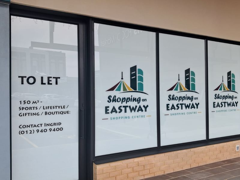A retail storefront unit featuring large glass windows and a brick base, currently available for lease at Shopping on Eastway.
