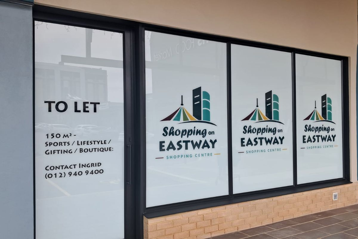 A retail storefront unit featuring large glass windows and a brick base, currently available for lease at Shopping on Eastway.