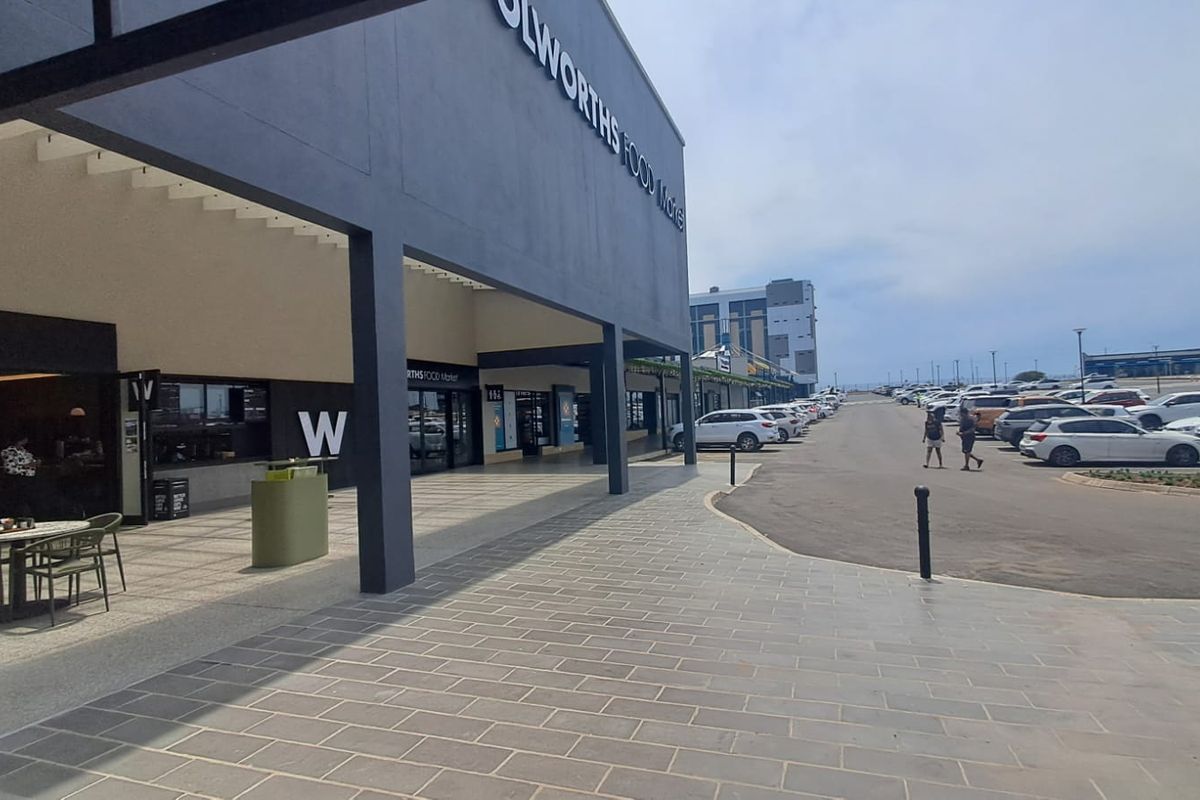 Exterior view of a modern retail storefront with a covered walkway, paved pedestrian area, and adjacent asphalt parking lot.