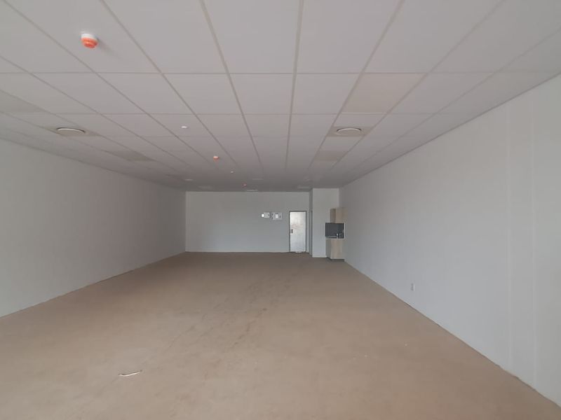 A spacious, open-plan retail unit featuring a suspended ceiling, recessed lighting, and a small built-in kitchenette area.