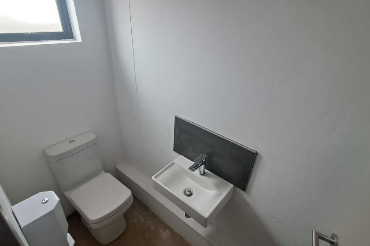 A clean and minimalist guest bathroom featuring a modern wall-mounted basin with a mixer tap and a standard toilet.