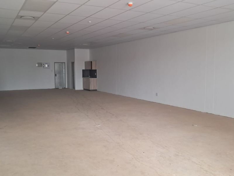 A spacious, empty open-plan retail unit featuring a suspended ceiling, a small built-in kitchenette, and concrete flooring, ready for custom fit-out.