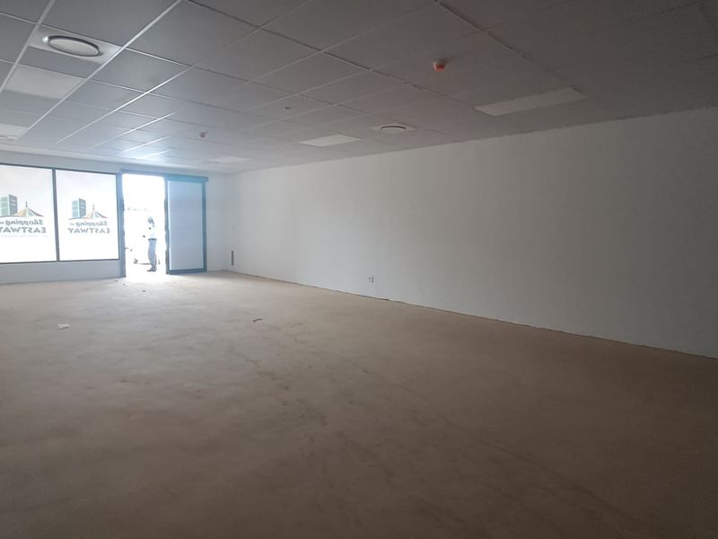 A spacious, vacant open-plan retail unit featuring a suspended ceiling, recessed lighting, and large display windows, offering a versatile layout for various business needs.