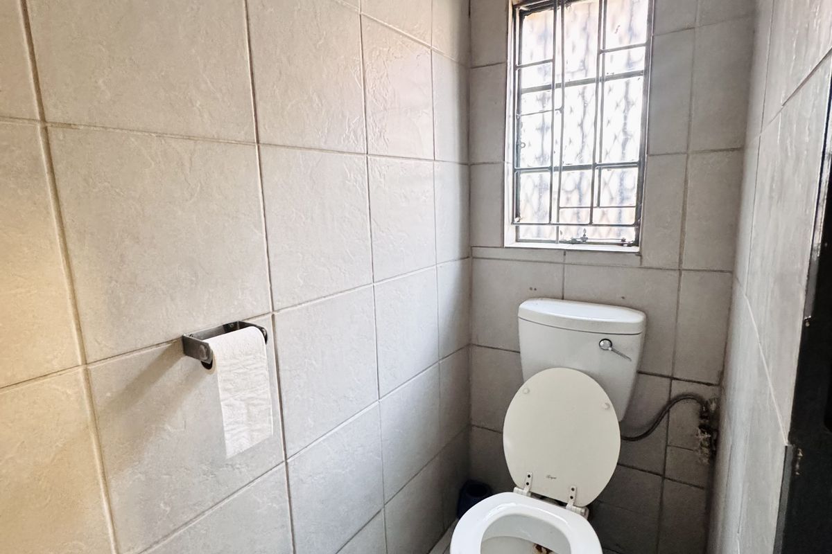 A compact guest bathroom featuring floor-to-ceiling wall tiles, a standard toilet, and a window with security bars.