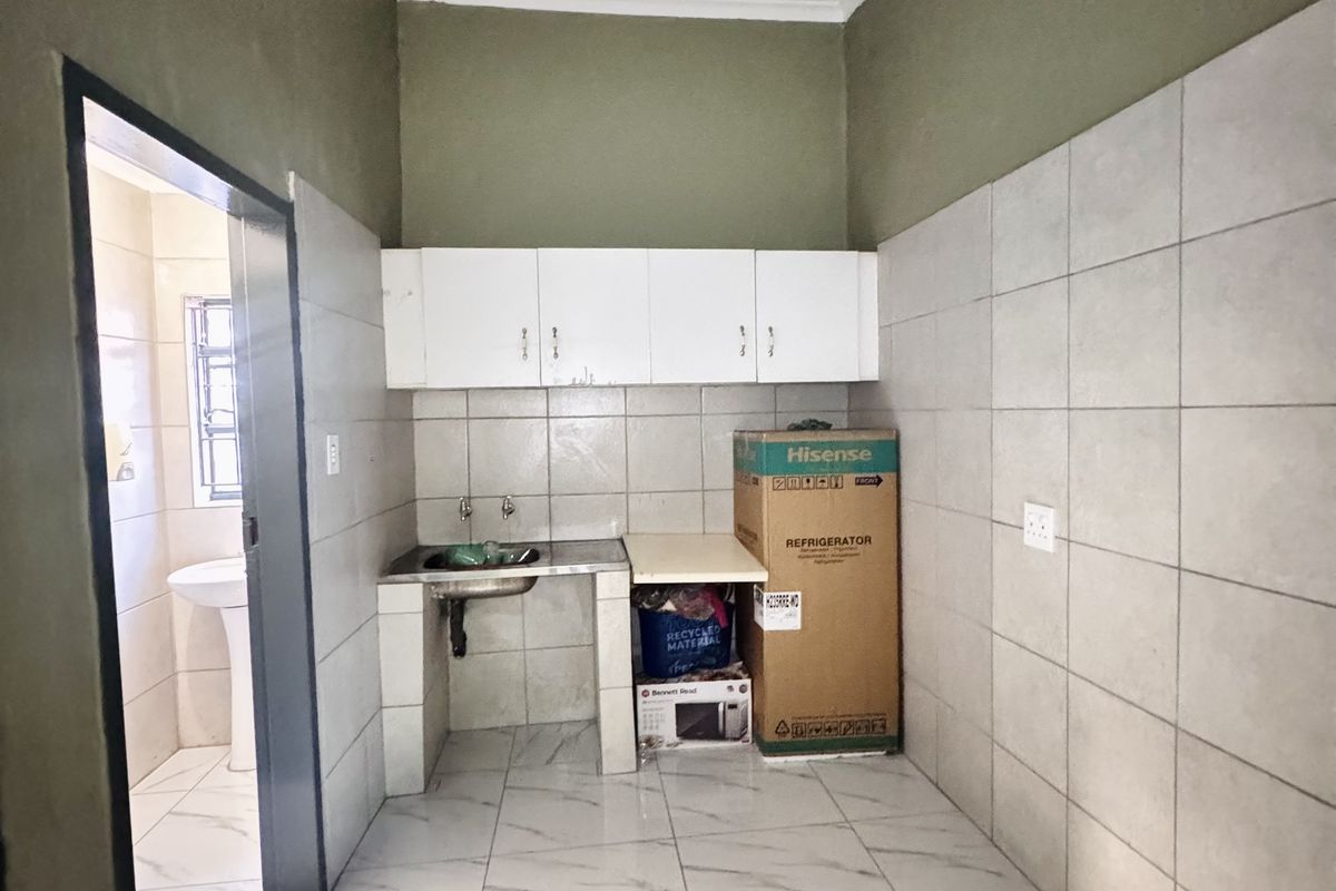 A compact kitchen area featuring tiled walls and flooring, built-in upper cabinetry, and a single basin sink with an adjacent utility space.