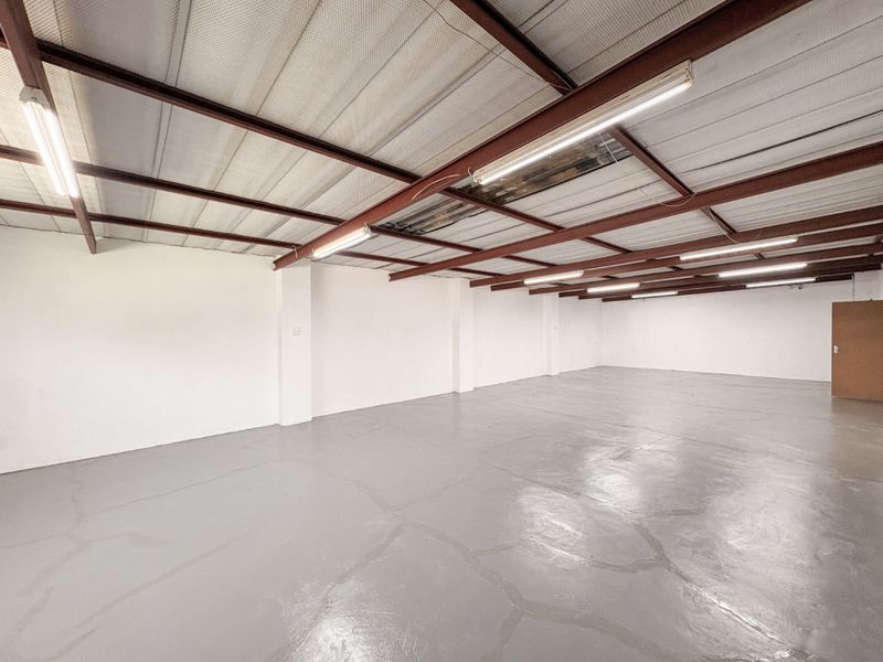 Spacious industrial utility area featuring exposed steel roof trusses, fluorescent lighting, and a durable painted concrete floor.