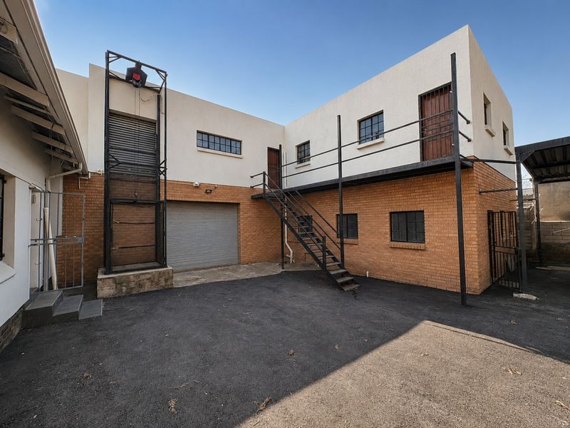 Rear industrial yard featuring a roller shutter door, external metal staircase, and integrated hoist system, providing functional access to the upper level.