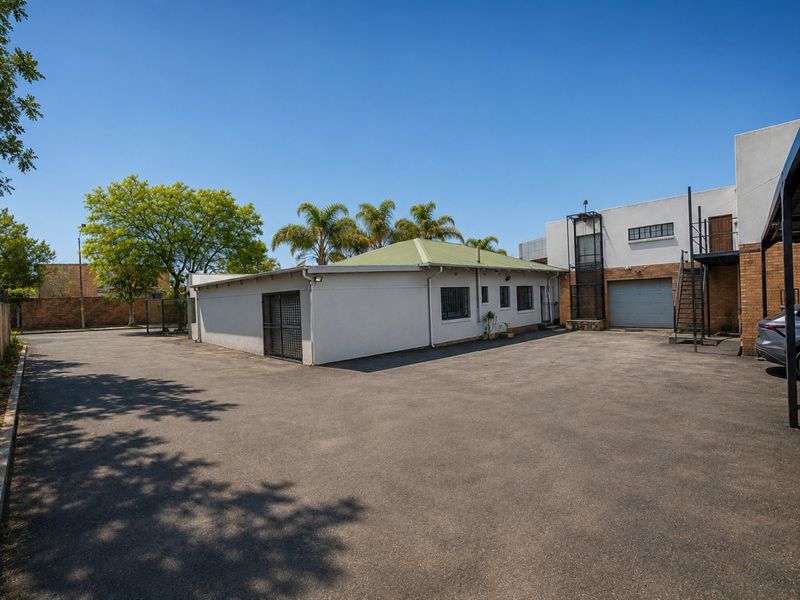 Rear exterior view of the industrial property featuring a large asphalt yard, secure access gates, roller shutter door, and external metal staircase access.